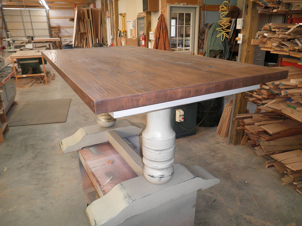 A handcrafted wooden table with a thick top and a sturdy, ornate pedestal base.